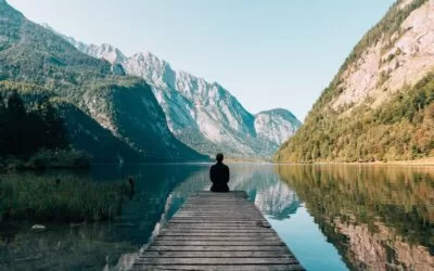 A person sitting on the end of a pier and looking out at a lake