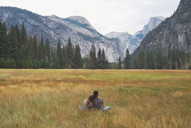 A couple sitting in a field and looking out towards the mountains