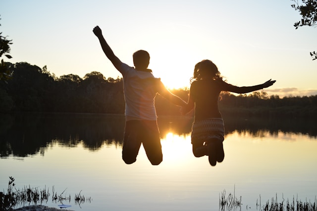 Silhouettes of a man and woman jumping against a background of a setting sun across a lake