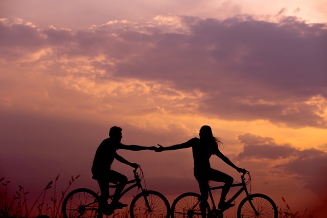 Silhouette of a couple riding bikes and holding hands