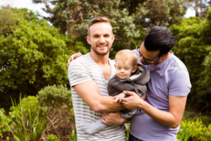 A gay couple smiling and holding a baby